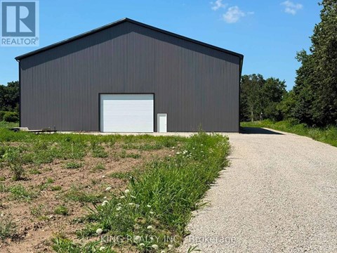 A large black building with a white door and a gravel driveway in front.