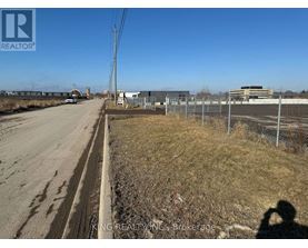 A road with a fence on the right side and buildings in the distance.