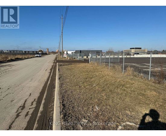 A road with a fence on the right side and buildings in the distance.