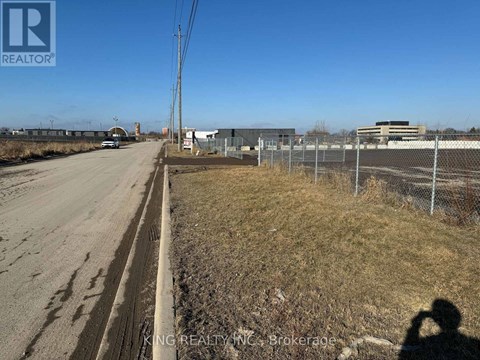 A road with a fence on the right side and buildings in the distance.