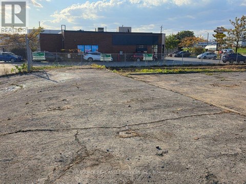 A parking lot with a building in the background and a fence in the foreground.
