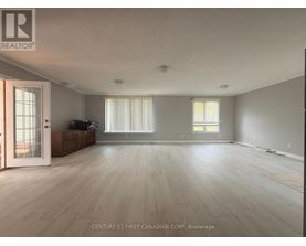 A spacious room with wooden flooring and a large window with blinds.