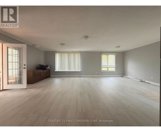 A spacious room with wooden flooring and a large window with blinds.