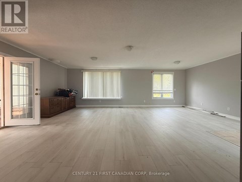 A spacious room with wooden flooring and a large window with blinds.