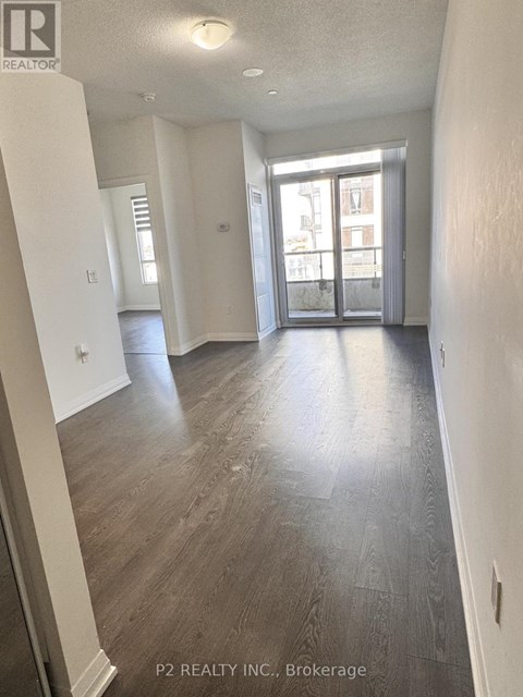 A spacious room with wood flooring and a large window.