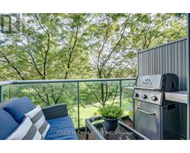 A stainless steel BBQ grill on a balcony with a cushioned chair and pillows.