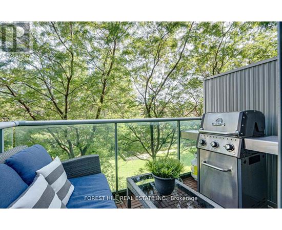 A stainless steel BBQ grill on a balcony with a cushioned chair and pillows.