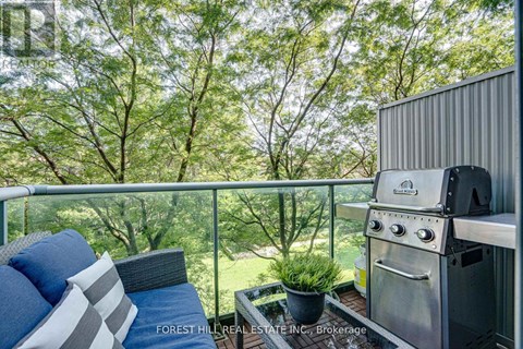 A stainless steel BBQ grill on a balcony with a cushioned chair and pillows.