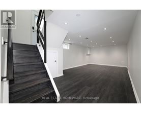 A spacious empty room with wooden floors and a staircase.