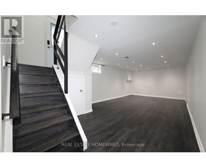 A spacious empty room with wooden floors and a staircase.