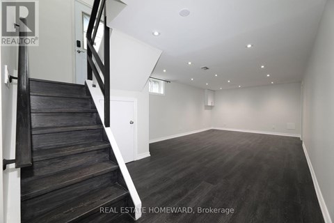 A spacious empty room with wooden floors and a staircase.