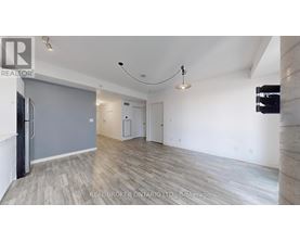A spacious room with wooden flooring and white walls, furnished with a grey sofa and a black refrigerator.