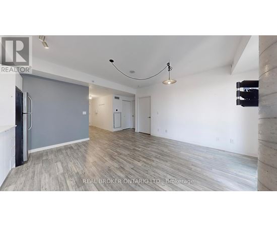 A spacious room with wooden flooring and white walls, furnished with a grey sofa and a black refrigerator.