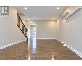 A spacious room with wooden flooring and a staircase.