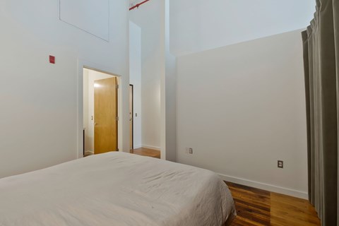 A white bed in a room with a wooden floor and a white wall.