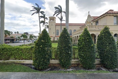 A large building with a clock tower is surrounded by trees and bushes.