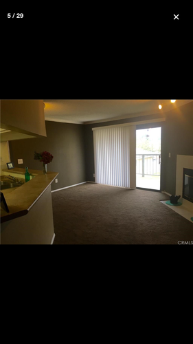 A room with a carpeted floor and a window with blinds.