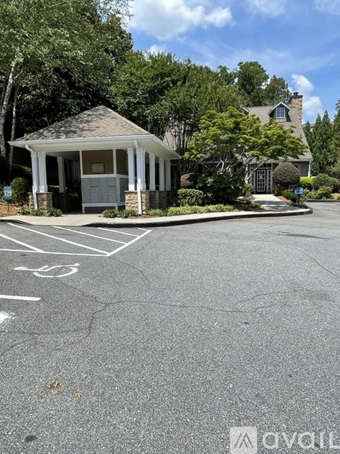 A gazebo is in front of a house with a parking lot in the foreground.