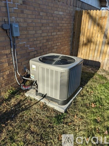 An outdoor air conditioning unit is installed on a grassy area next to a brick wall.