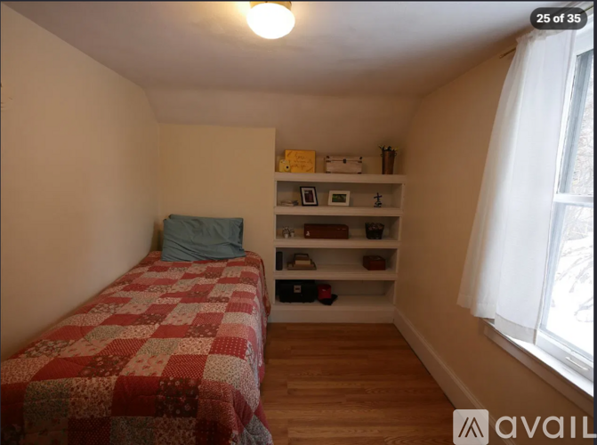 A bedroom with a bed, a window, and a shelf with various items.