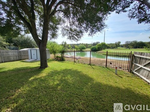 A backyard with a tree, a fence, and a pool.