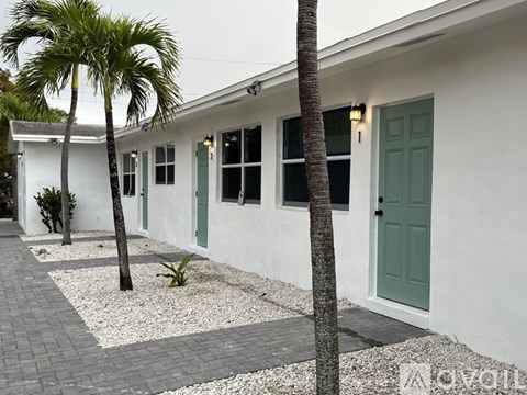 A white house with a green door and a palm tree in front.