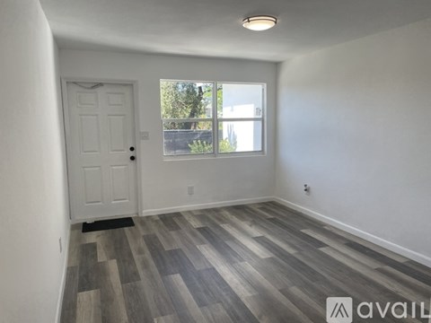 A room with a white door and a window with a view of trees and a building outside.