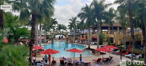 A pool surrounded by palm trees and people relaxing by the poolside.