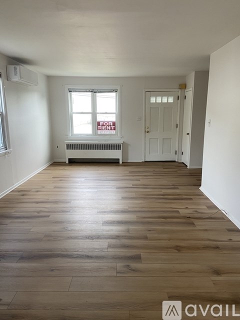 A room with wooden floors and a window with a "For Rent" sign.