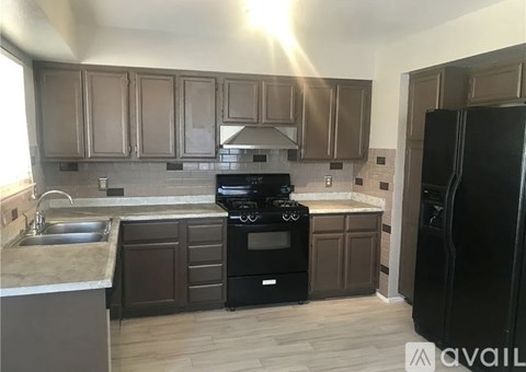 A kitchen with brown cabinets and a black refrigerator.