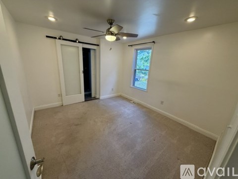 A room with a ceiling fan and a window with a view of trees.