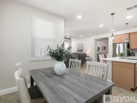 A dining room with a table and chairs and a plant in a white vase.