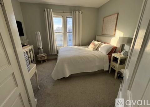 A bedroom with a large bed and a window with curtains.