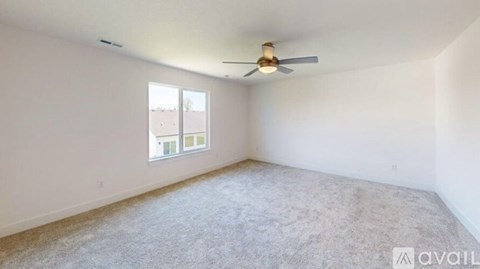 A room with a carpeted floor, a ceiling fan, and a window with a view of buildings outside.