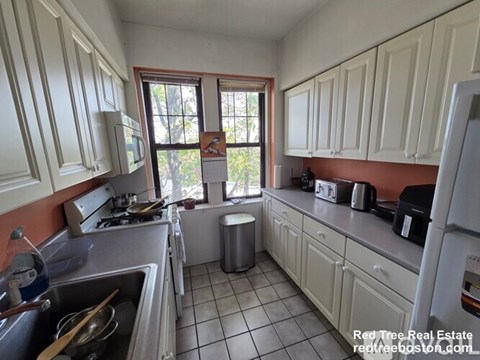 A kitchen with white cabinets and a red wall.