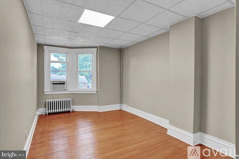 A room with wooden floors and a window with a view of trees and a building outside.