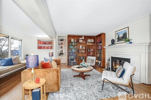A living room with a fireplace, a chair, a couch, a table, and a bookshelf.