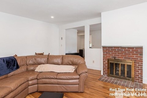 A living room with a brown leather couch and a brick fireplace.