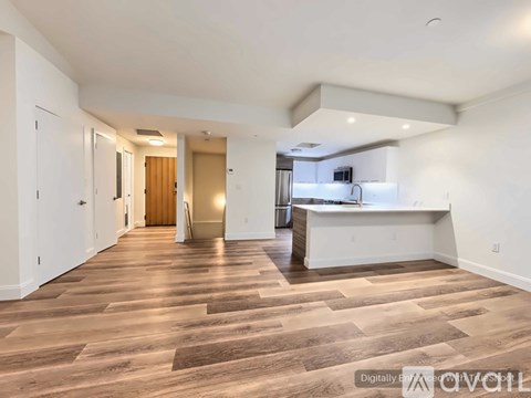 A spacious room with wooden flooring and a kitchen area in the background.