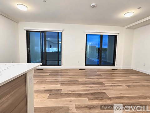 A room with wooden flooring and white walls, featuring a kitchen island and sliding glass doors.