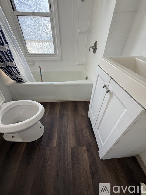 A white toilet sits in a bathroom with a wooden floor and a window.