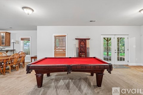 A pool table is in the middle of a room with a wooden floor and a carpet.
