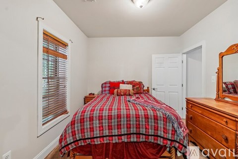A bedroom with a bed covered in a red and black plaid comforter.