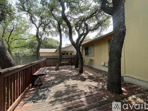 A wooden deck with a bench and trees in front of a house.