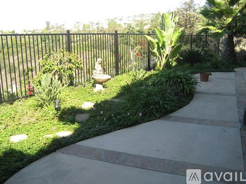 A garden with a statue, a fence, and a paved walkway.