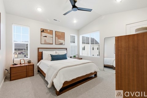 A bedroom with a large bed, a ceiling fan, and a view of a cityscape through the window.