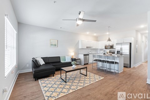 A living room with a black couch and a coffee table in front of a kitchen.