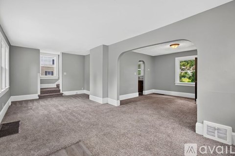A spacious room with grey carpeting and a window overlooking a tree.