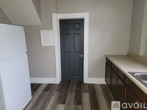 A kitchen with a white fridge, a black door and wooden flooring.