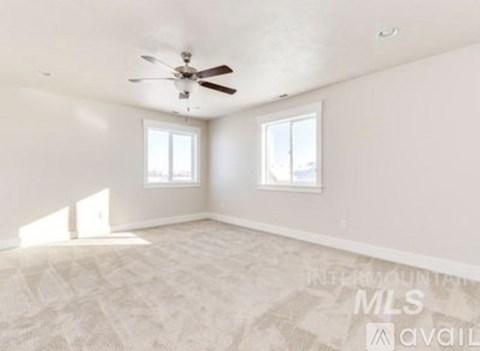 A spacious room with a ceiling fan and two windows.